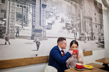 Newlyweds sitting on table at cafe with two cups of coffee