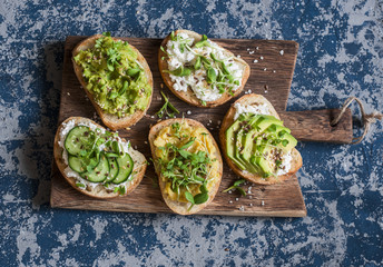 Wall Mural - Healthy sandwiches with avocado, hummus, ricotta, cucumber, sunflower sprouts, micro greens and flax seeds. On a wooden cutting board, top view. Healthy vegetarian snack