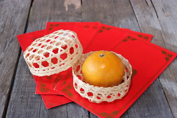 Orange in a basket on old wooden board with Chinese red envelope packet or ang pao background. Happy Chinese new year concept.