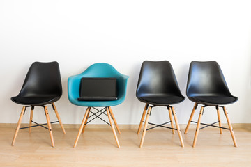 The laptop on a chair. Blue chair among black on a white backgro