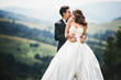 Bride leans to groom while he hugs her from behind and kisses te