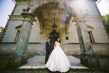 Wall Mural - Bride in luxurious dress goes away from man standing under the s