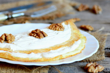 Wall Mural - Egg omelette with sweet filling on the plate. Hearty omelette with soft cheese and walnuts. Fork, knife, raw shelled walnuts on a wooden background. Closeup