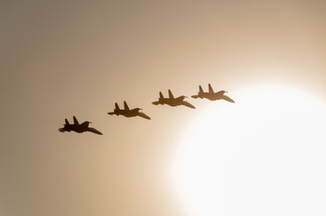 4 Su-27 Flanker jet fighters fly in back lit against cloudy sky background
