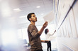 © Mint Images - A woman and a man standing in an office adding pieces of paper to a display on a wall.