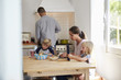 © Monkey Business - Kids and mum at table, dad cooking, three quarter length
