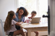 © Monkey Business - Mum sitting with kids at kitchen table, son using laptop