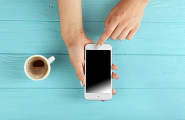 Wall Mural - Female hands with smartphone and cup of coffee on wooden background