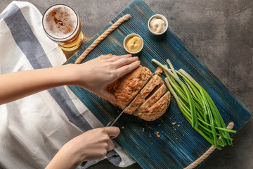 Wall Mural - Woman hands cutting tasty loaf of beer bread on wooden board