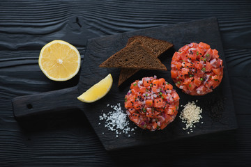 Wall Mural - Serving board with salmon tartars over black wooden background