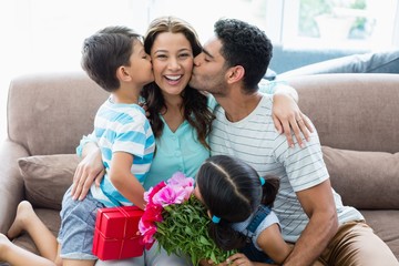 Wall Mural - Woman receiving kiss from his husband and kids in living room