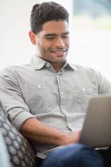 Canvas Print - Man sitting on sofa and using laptop in living room