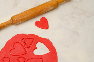 Red dough with a rolling pin and cut out hearts on a white table, close-up. Space for text