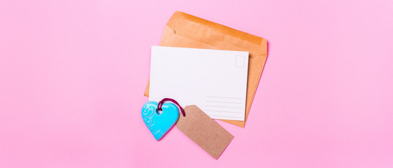 Wall Mural - empty postcard love letter with envelope and blue turquoise heart on a pink background