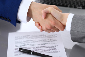 Businessman and business woman shaking hands to each other above signed contract