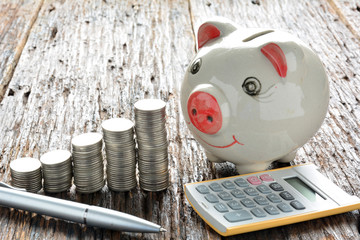 Finance stack coins, calculator, silver pen and piggy bank on wood table and copy space