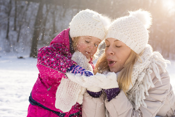 Mother having fun with daughter while blowing snowflakes off her hands