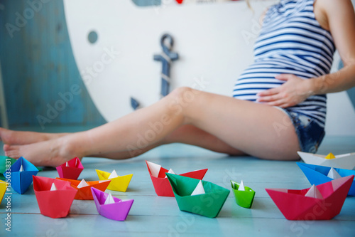 Pregnant Girl Sitting On The Floor Next To The Colored Paper Boats