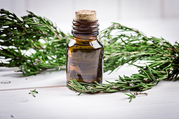 Rosemary essential oil on a  bottle with  fresh rosemary on wooden background, selective focus.