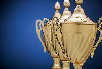 row of three gold trophy cups on blue