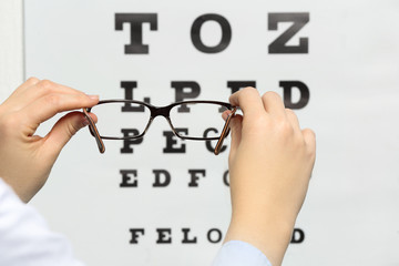 Wall Mural - Young woman holding spectacles on eyesight test chart background, closeup