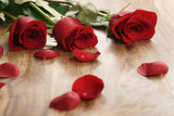 Fototapeta Kwiaty - three red roses and petals on old wood table, romantic background