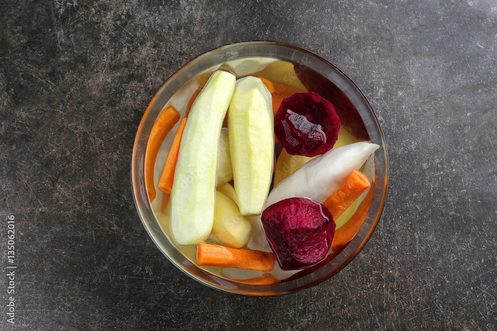 Bowl with freshly peeled vegetables on grey background