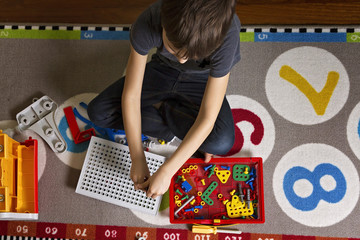 Wall Mural - Child playing with toys tool kit while sitting on the floor in his room.Top view