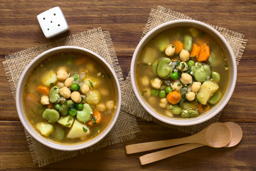 Wall Mural - Vegetarian chickpea soup with carrot, broad bean (fava bean), pea, potato, onion, garlic and parsley served in bowls, photographed overhead on wood with natural light
