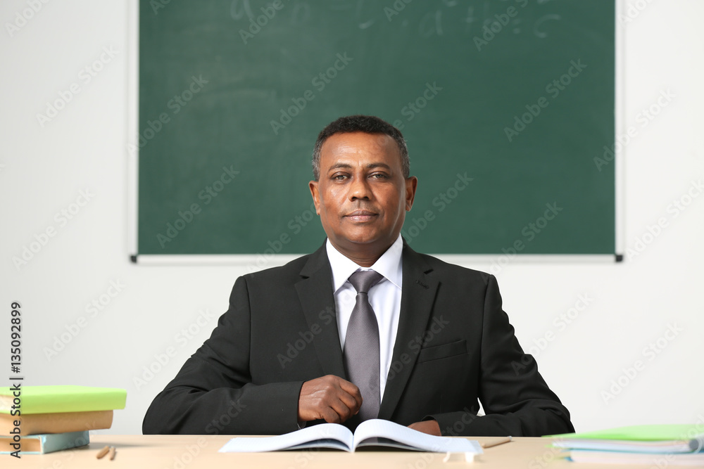 Confident Indian teacher sitting at table in classroom