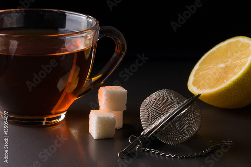 Fotografia, Obraz cup of tea with a strainer and lemon on dark background