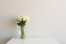 Cream Roses In Glass Vase On White Table Against Neutral Wall