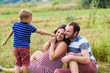 © o_lypa - Child tickles his pregnant mother a blade of grass. Mother is expecting a baby. Pregnant woman, husband and their son playing outdoors.