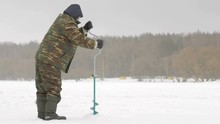 Winter Fishing On River. A Man Drills A Hole In Ice.