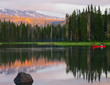 A bright red canoe on a high mountain lake with the forest and mountains reflecting on the calm waters and the orange glow of sunset on a peaceful summer evening. 