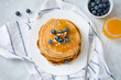 Stack of pancakes with blueberries, walnuts and honey served on white plate over gray background. Top view