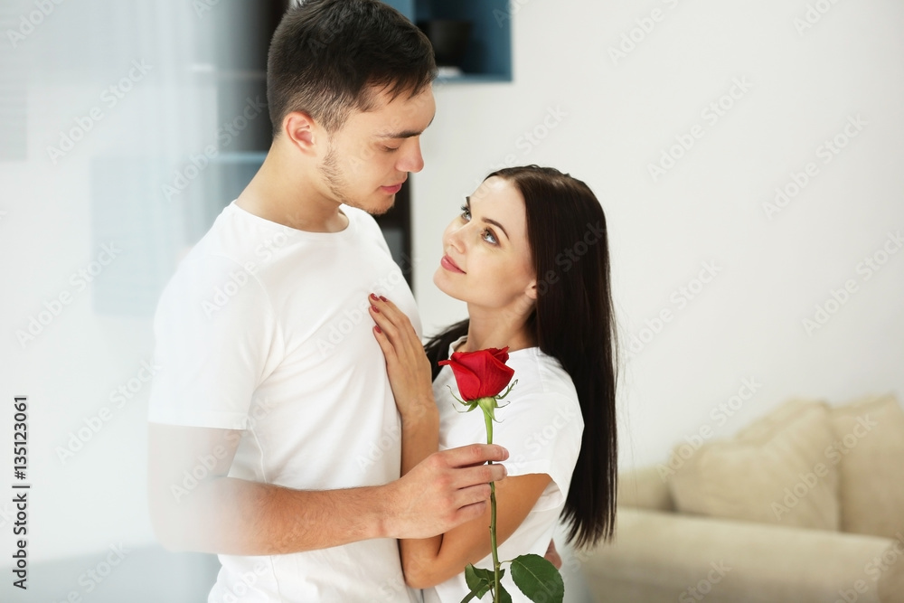 Man presenting red rose to girlfriend at home