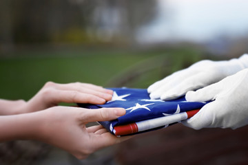 Hands holding folded American flag on blurred background