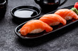 Salmon sushi with soy sauce on a black plate and dark concrete background.