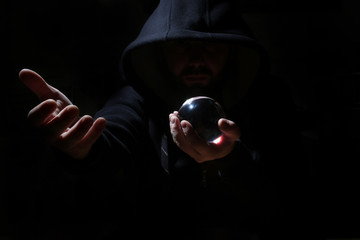 man in a black hood with cristal ball