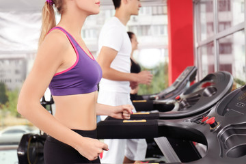 Wall Mural - Young sporty woman running on treadmill in gym, close up view