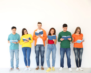 Wall Mural - Group of people reading books while standing near light wall