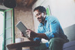 © SFIO CRACHO - Bearded smiling African man using tablet for video conversation while relaxing on sofa in modern office.Concept of young business people working at home.Blurred background.Selective focus.