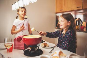 Two kid girls eating swiss  fondue for dinner