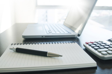 Office workplace with pen, notebook, calculator and computer lap