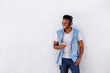 © mimagephotos - smiling man with headphones and cellphone standing by white wall