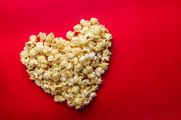 Cinema concept of popcorn arranged in a heart shape on red backg