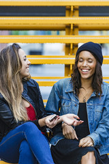 two mixed race female friends sitting and using a smartphone