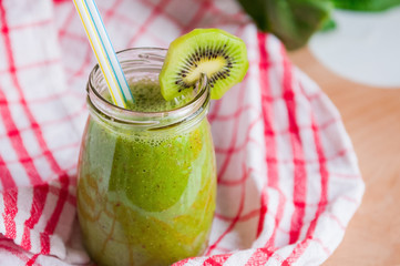 Homemade Healthy green smoothie with spinach and kiwi in a jar mug with a straws on a checkered napkin and a wooden board. Selective focus