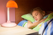 © madhourse - Seven-year girl asleep in bed, reading lamp is included on the next table